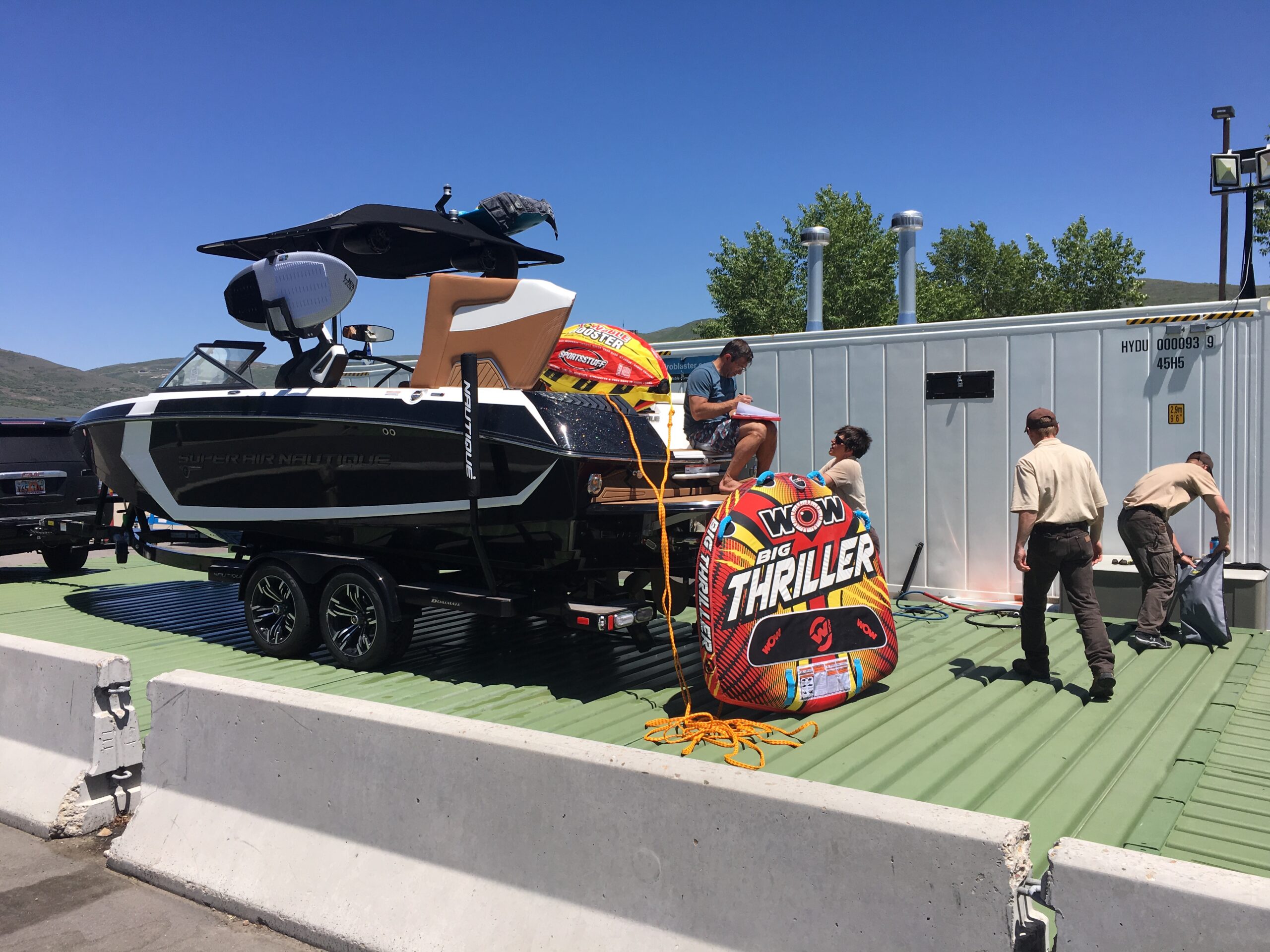 A black boat and inflatable tubes are inspected by people and park rangers at a boat ramp.