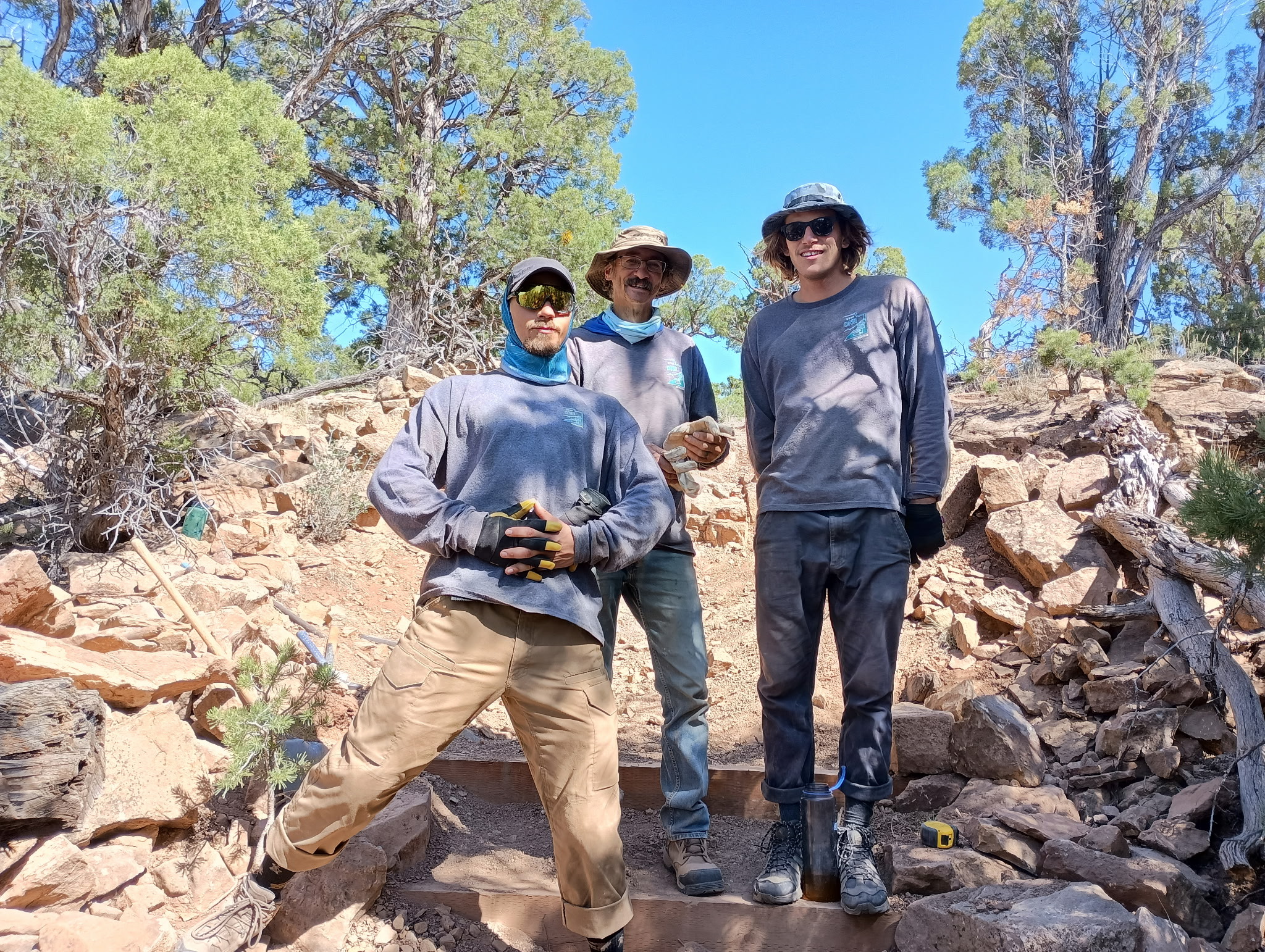 Three trail crew technicians standing outside in Moab. They are all wearing clothing that shows they have been outside working